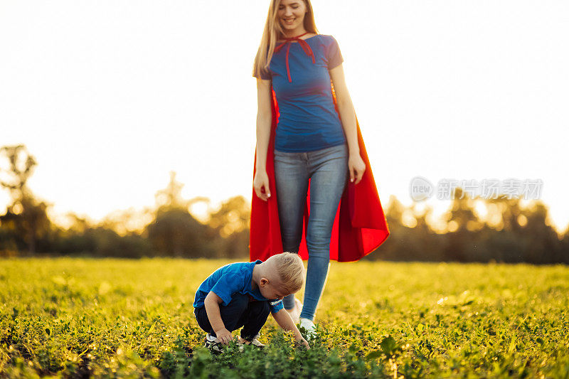 幸福的家庭，妈妈和她的小儿子穿着超级英雄的服装，在阳光明媚的日子里在户外种一棵树苗