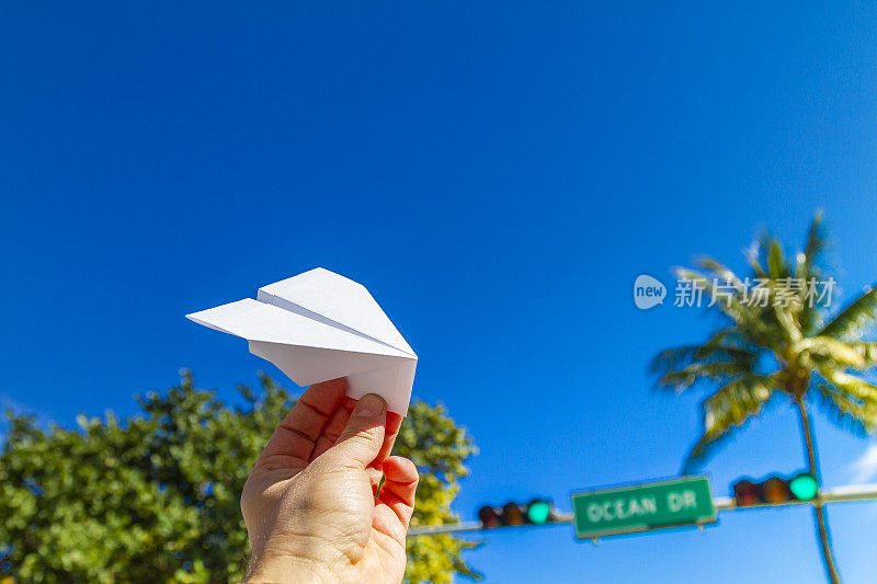 一名年轻的旅行男性在美国南佛罗里达州迈阿密海滩南海滩的海洋大道前玩纸飞机，享受他的假期。旅行的概念。