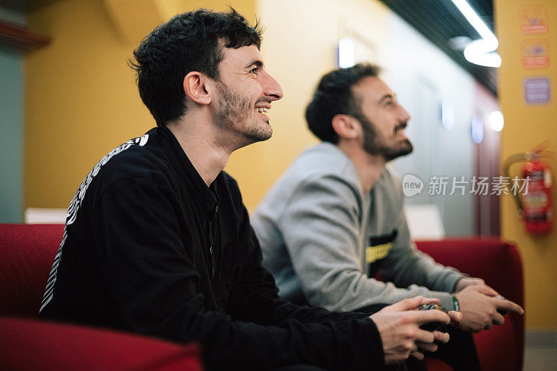男性画像的两个胡子男人谁玩电子游戏在室内的数字游戏机。手里拿着手柄的人。Xbox和Playstation概念摄影。