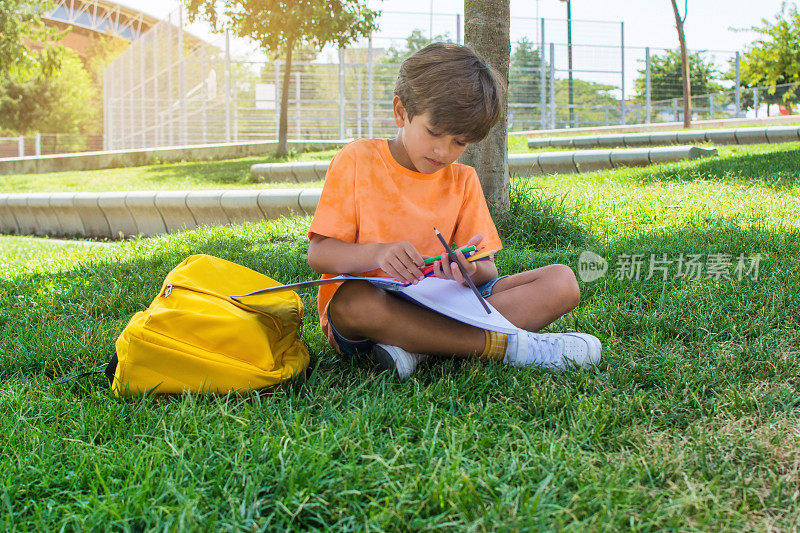 学龄前儿童在操场上做作业，坐在草地上。