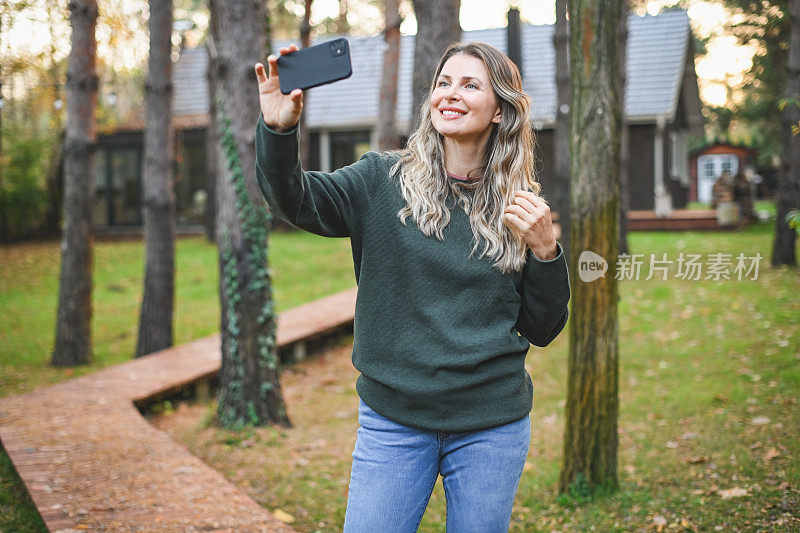 美丽的女人走在她的小屋花园拿着手机