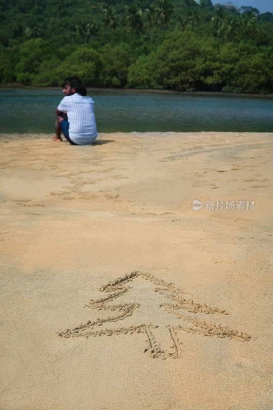 圣诞树的图像画在沙滩上的沙滩上阳光明媚的水边，印度人坐在海边的背景，重点在前景，圣诞节在南半球的概念