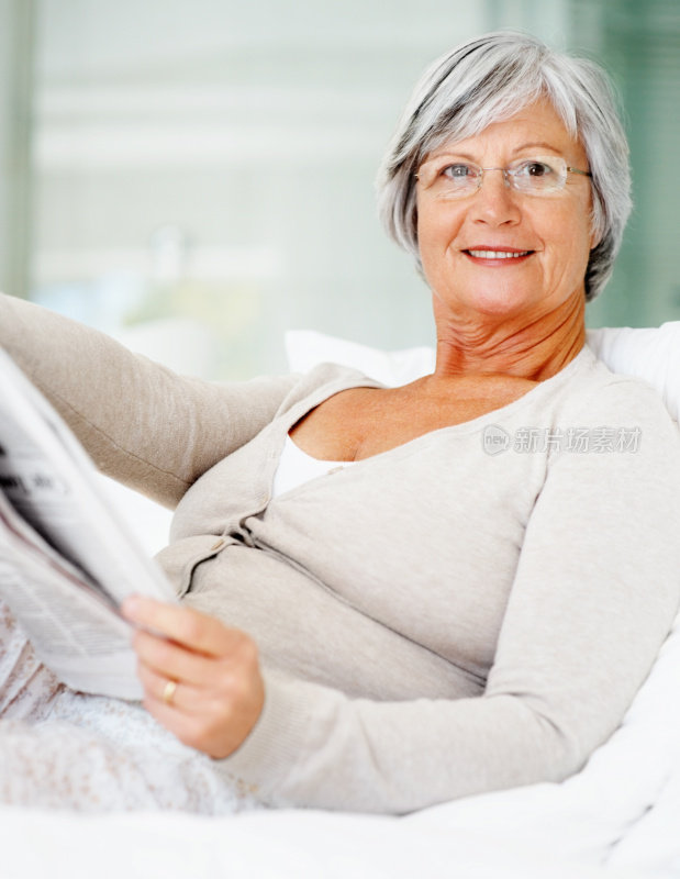 放松的老妇人在家里的床上看报纸