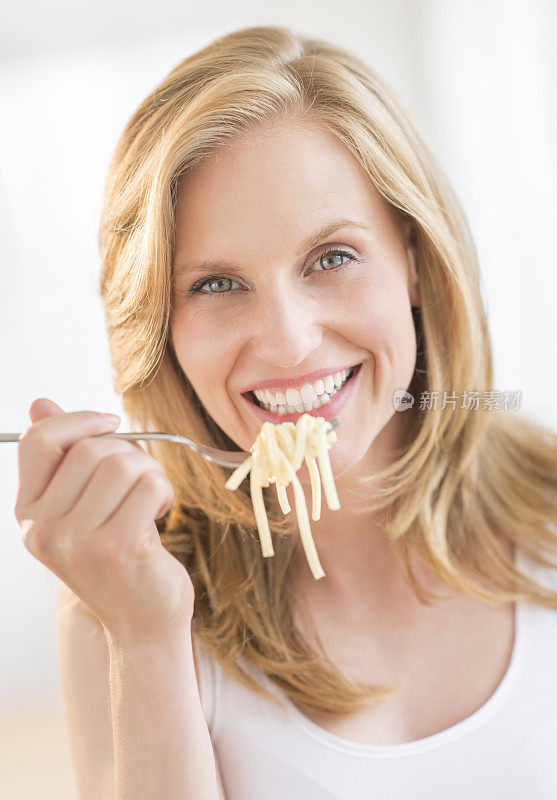 年轻女子在家里拿着叉子吃意大利面