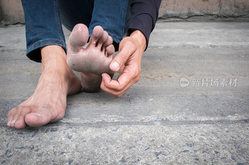 一个男人坐在旧水泥地板上的脏脚。