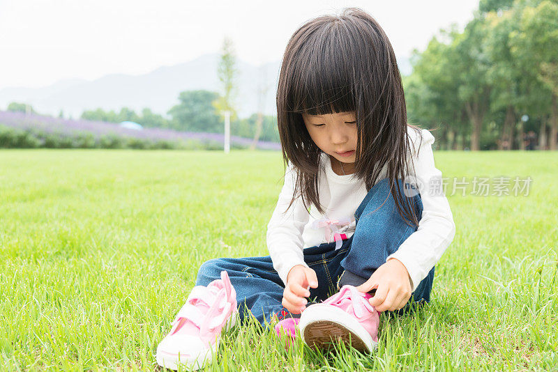 小女孩坐在草地上，系好鞋带