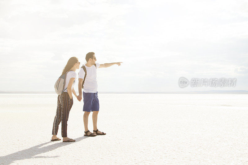 夏日情侣在日落时在盐湖上牵着手。