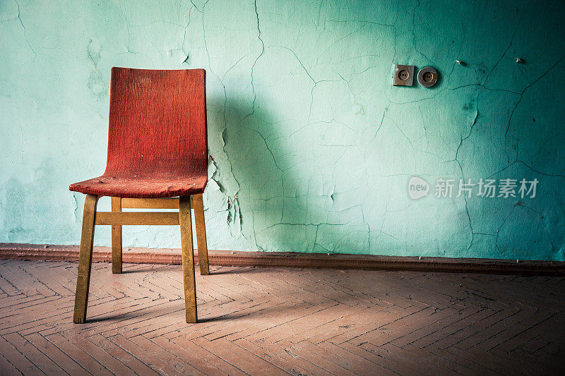 一张红色的椅子靠在一堵旧的绿色墙壁上
