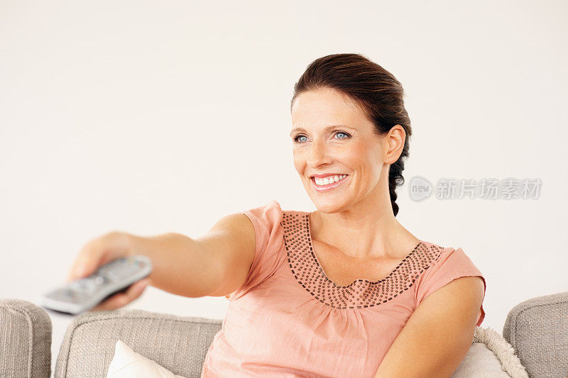 微笑的女人用遥控器换电视频道