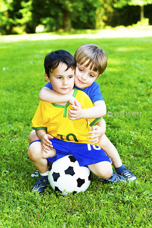 两个蹒跚学步的孩子坐在足球上拥抱