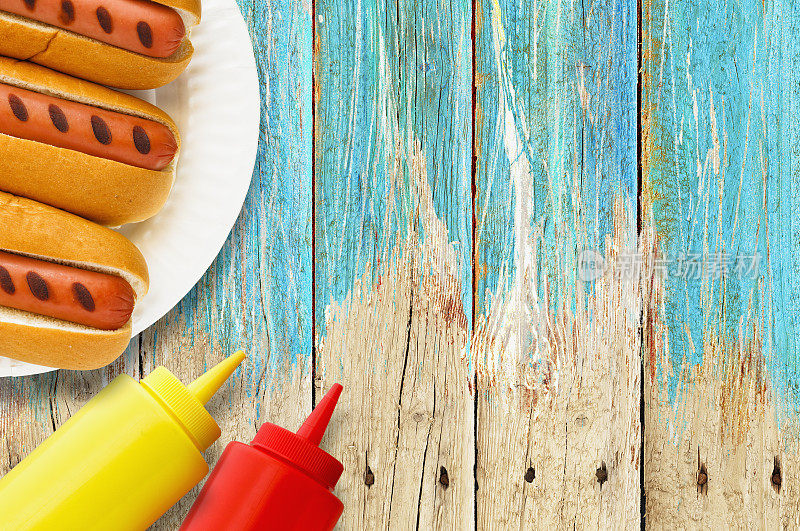 烤热狗，纸盘子，番茄酱，芥末瓶子，野餐桌上
