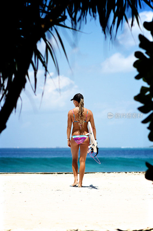冲浪者女孩带着她的冲浪板走向海滩