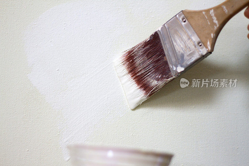 手用油漆刷蘸湿白色油漆，油漆杯