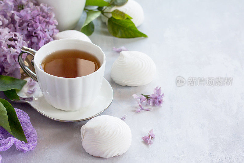 精致的香草棉花糖放在精致的白色盘子里。有棉花糖的静物画，一杯茶和紫丁香，背景是古老的石头。副本的空间。