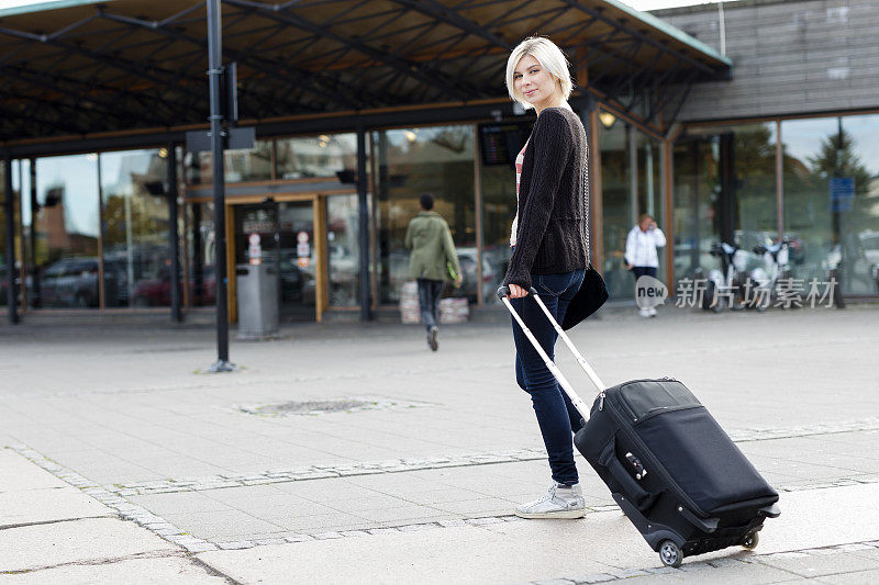 微笑的年轻女子带着一个轮式行李箱旅行