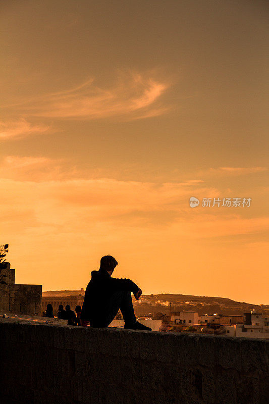 孤独的年轻人坐在墙上看日落看风景