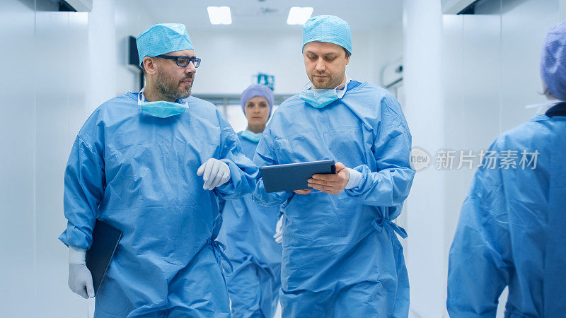 两位医生在医院里走来走去，讨论即将进行的手术。一个使用平板电脑在手中。