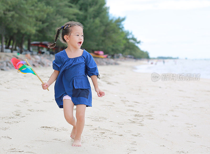 傍晚，小女孩抱着五颜六色的风车玩具在沙滩上玩耍。