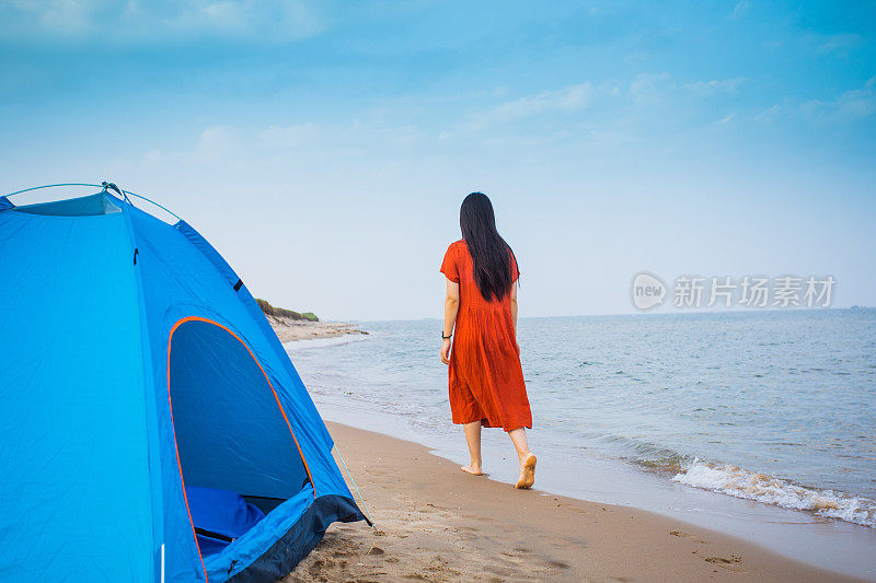 一名年轻女子在海滩上带着帐篷散步