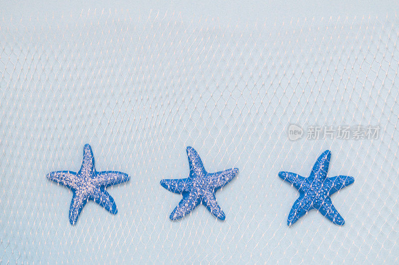 3只蓝色海星和渔网在粉彩背景上极简的概念。