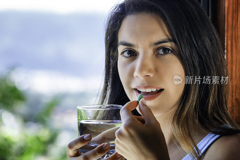 特写的西班牙年轻女子准备服用药丸与一杯水在手里