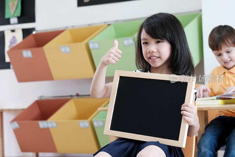 可爱的亚洲女孩手持空白黑板在幼儿园教室，儿童教育，学前概念