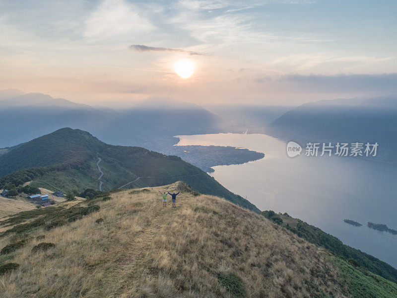 无人机航拍父亲和女儿在清晨徒步登山，拥抱大自然的清新，张开双臂等待成功