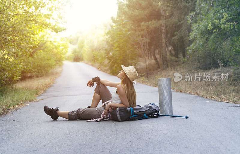 女旅人坐在路上，望着别处的路。背包徒步者在路上放松，欣赏日落