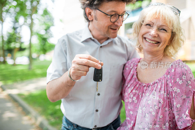 一对老年情侣抱在一起，手里拿着车钥匙站在外面