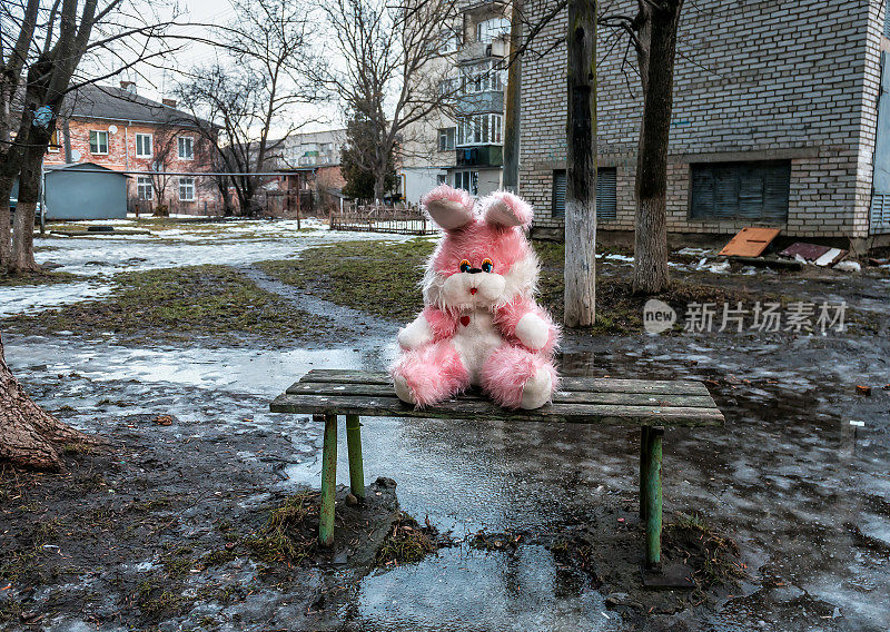 在糟糕的天气里，一只粉色长毛绒兔子坐在贫民区的长椅上