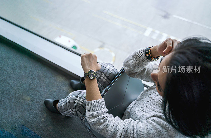 一名亚洲女子在机场候机楼等待航班，查看时间