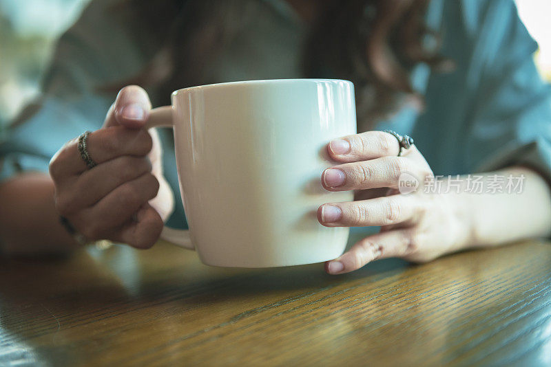 近距离的年轻女性的手拿着一个咖啡杯