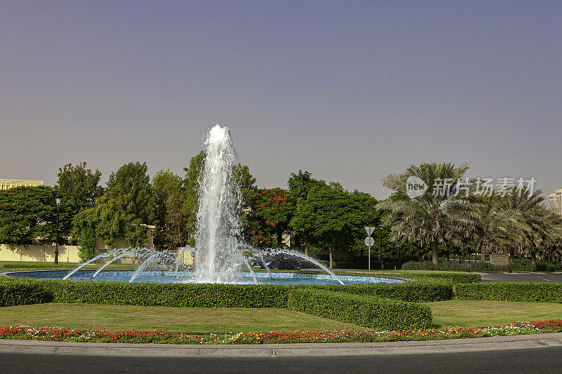 迪拜，阿拉伯联合酋长国-一个喷泉在城市草地地区，在早晨的阳光;在一个周五的早晨，当地的周末，只有一辆车在环形交叉路口。副本的空间。