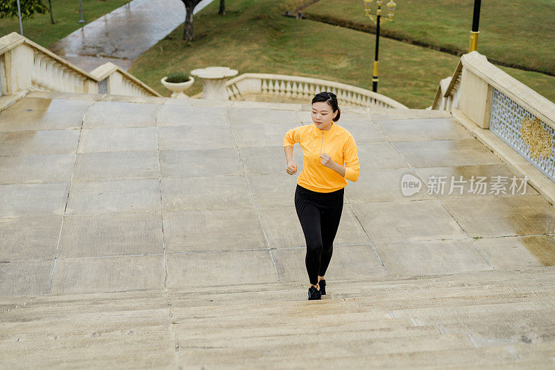 运动的年轻亚洲妇女在雨下的田径服爬楼梯