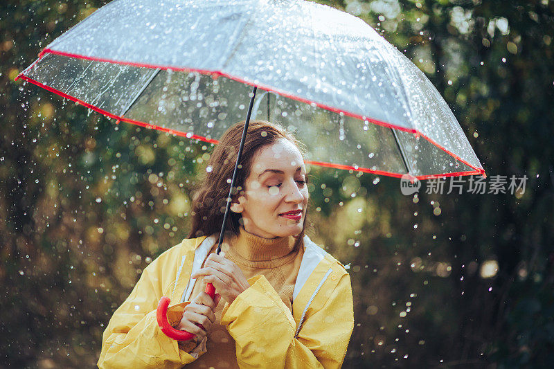 秋雨中带着透明塑料伞的快乐女人