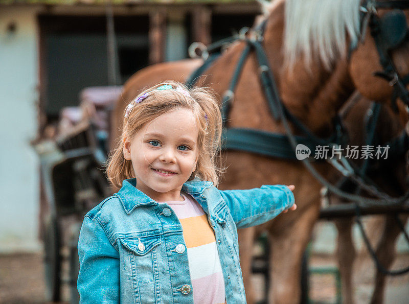 可爱的微笑小女孩和两匹马在一个马厩