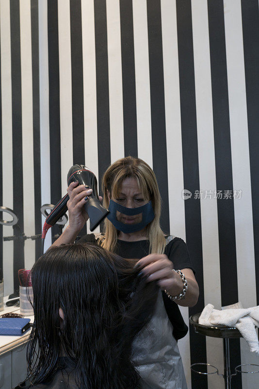 美发师在美发厅为顾客吹干头发。新常态。