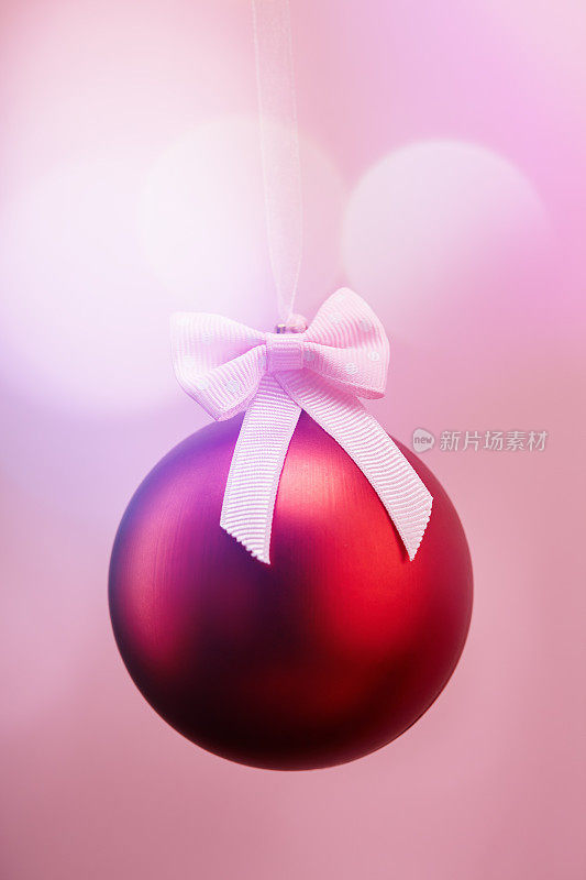 红色的圣诞球挂在蝴蝶结的丝带上，背景是柔和的散角球圈
