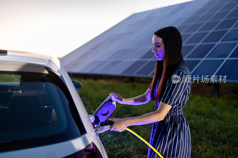 背景中为电动汽车和太阳能电池板充电的女性