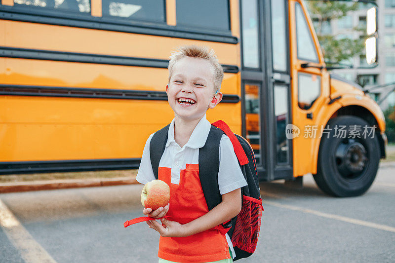 快乐的笑微笑的白人男孩学生乘坐黄色的公共汽车在九月的第一天。重听儿童在学校外面吃苹果水果。秋季教育和返校。