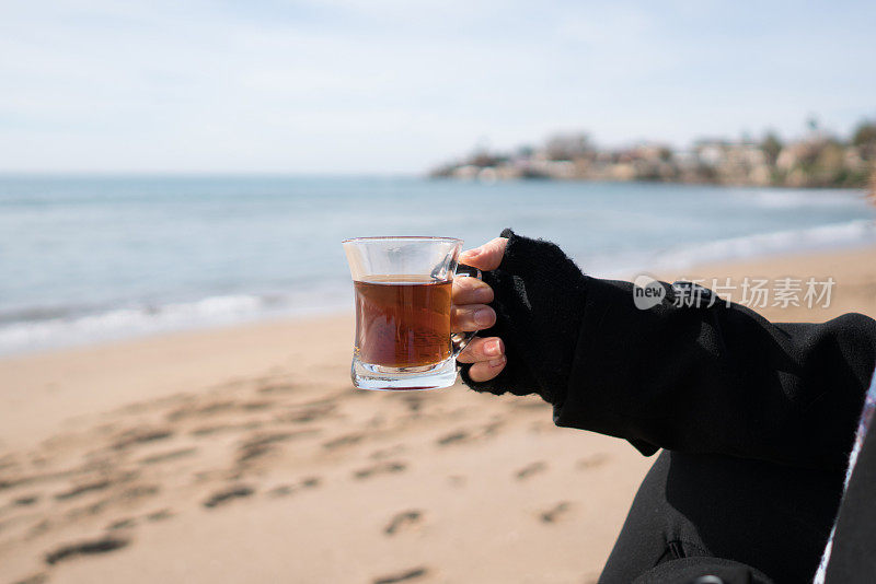 在海滩上拿着一杯茶的女士。