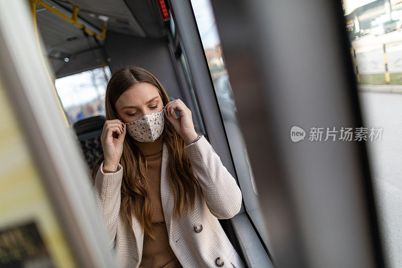 年轻的女商人在乘公共汽车上班时调整防护口罩