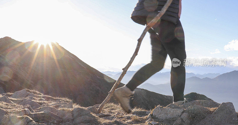 一名女徒步者拿着登山杖观看山上的日落