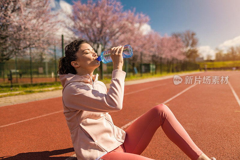 运动的年轻女子在运动轨道上跑步后喝水。