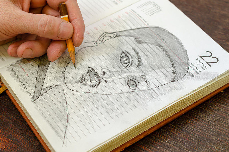 一名男子在一本打开的日记中用铅笔素描了一名年轻的成年男子。一个非裔美国人的黑白肖像。他的左手在纸上画了几笔。在室内。