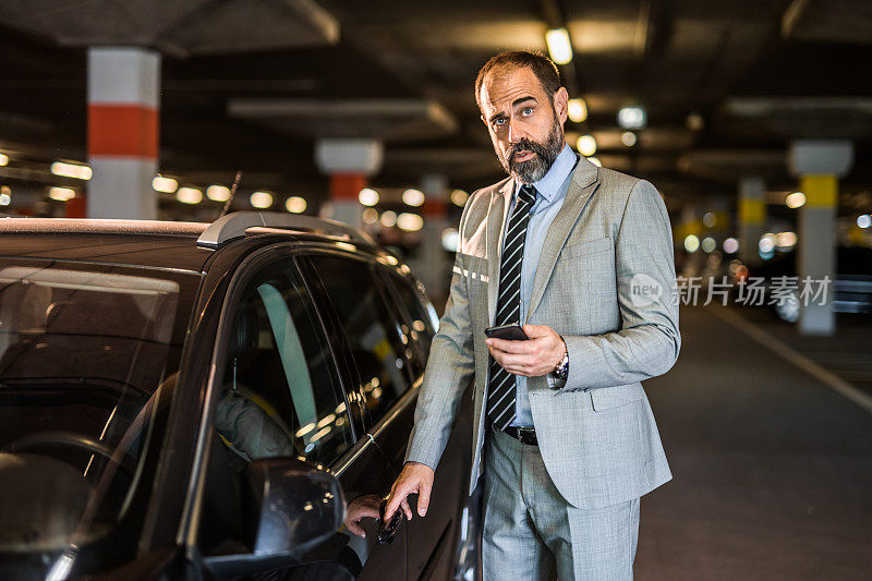 商人在停车场上他的车，用电话。