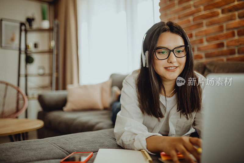 一位年轻的女学生坐在沙发上使用笔记本电脑耳机学习