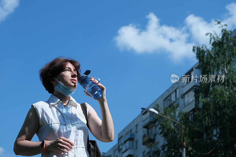 一个成熟的女人在炎热的夏天在城市的街道上喝水