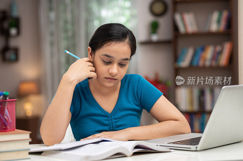 一个十几岁的女孩在家里学习的照片:-库存照片