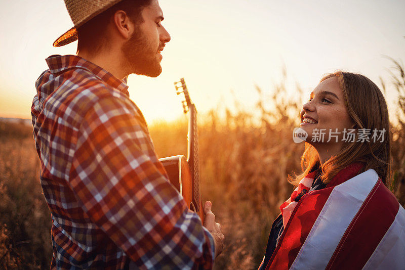 在日落时分，一个男人在球场上弹吉他，给他的女朋友唱歌